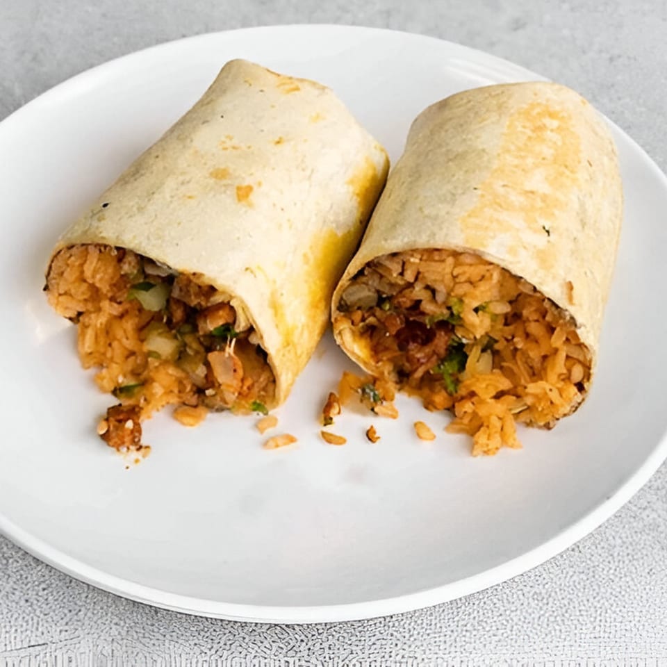 Two halves of a large burrito filled with orange rice and meat, on a white plate.