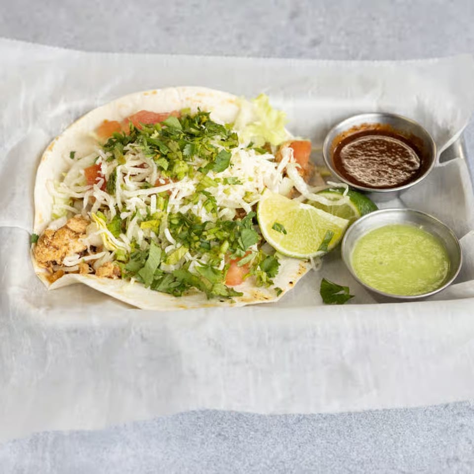 A Smack'n Tacos chicken taco with shredded cheese, lettuce, cilantro, and lime, with two sauces.