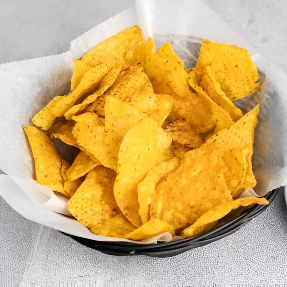 A black basket filled with crispy, golden tortilla chips lined with white parchment paper.