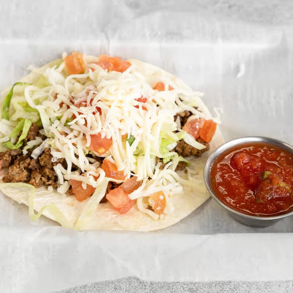 A Smack'n Tacos soft taco with ground beef, lettuce, cheese, and tomatoes, with a side of salsa.