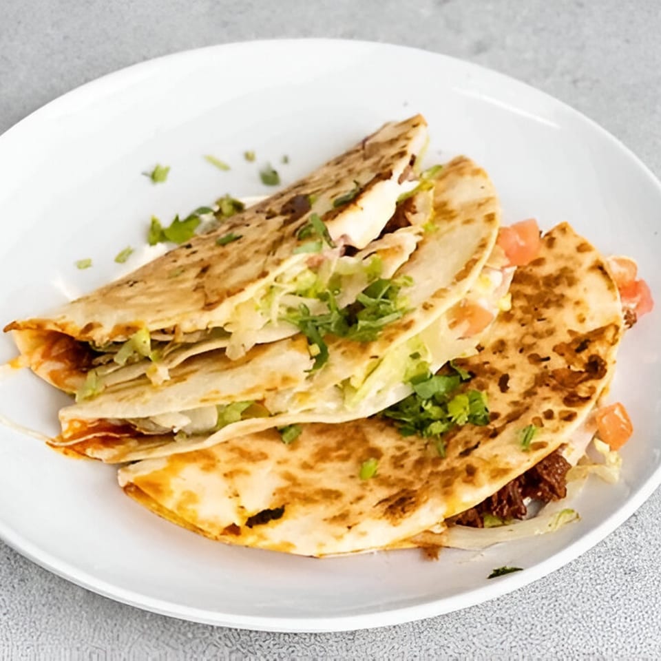 Three golden-brown quesadillas filled with meat, cheese, lettuce, and tomatoes, garnished with cilantro.